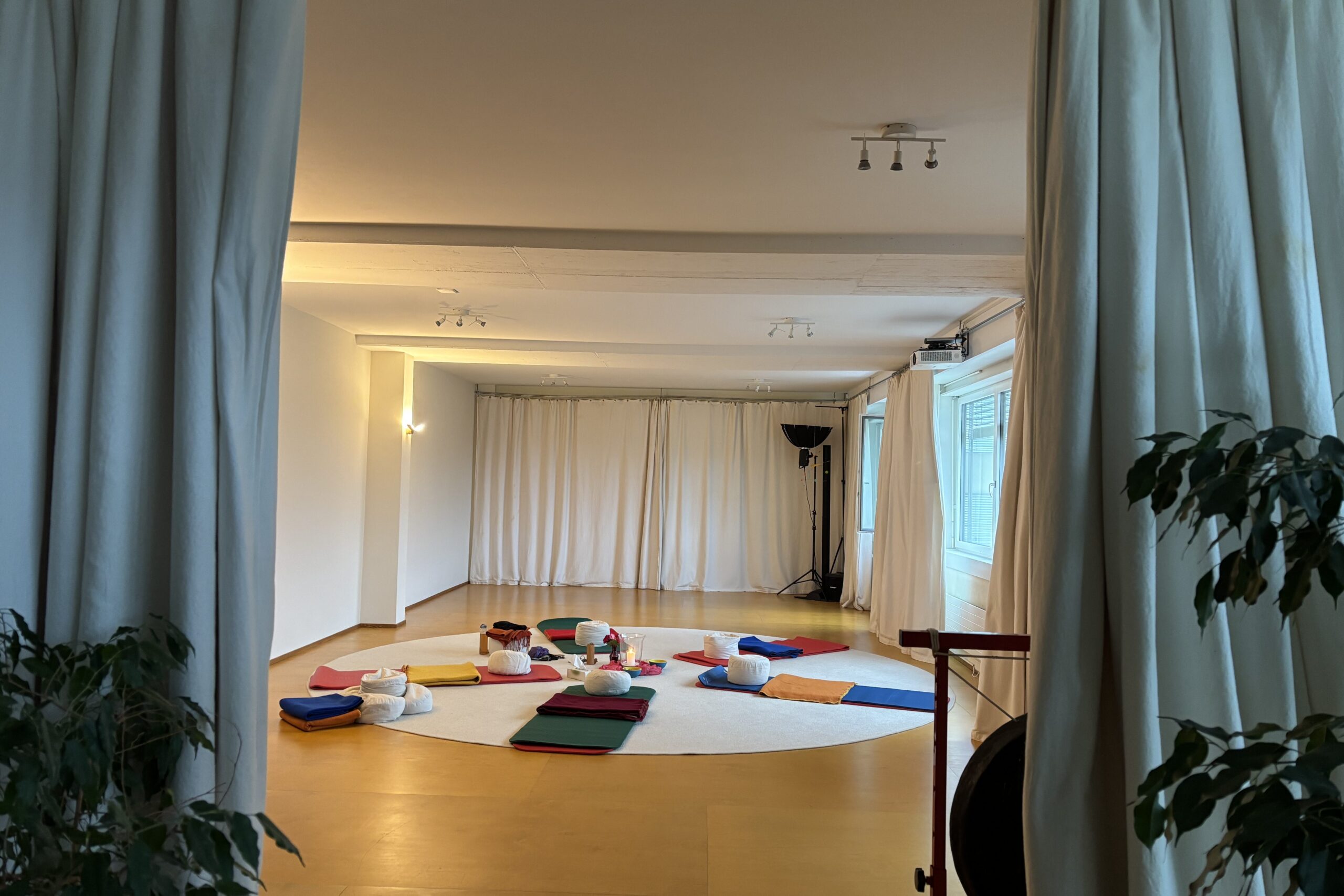 Blick durch Vorhänge in den Seminarraum in Luzern mit einem Kreis aus Matten und Sitzkissen