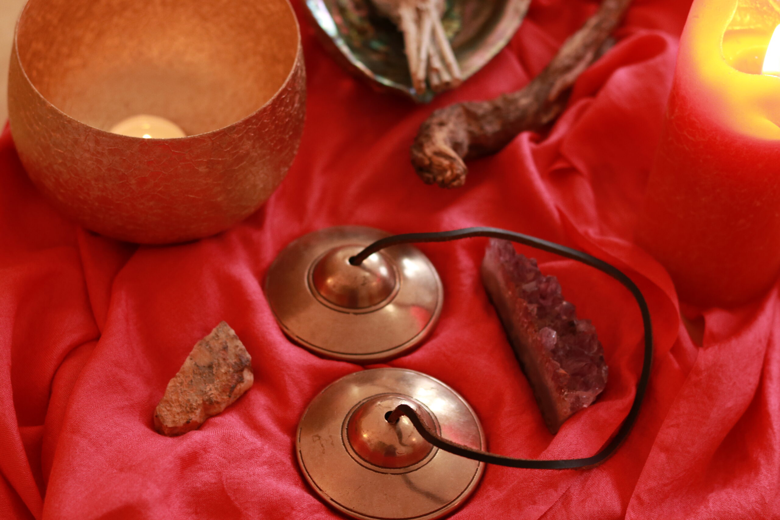 Zimbeln, Amethyst, Stein und goldenes Windlicht auf rotem Tuch